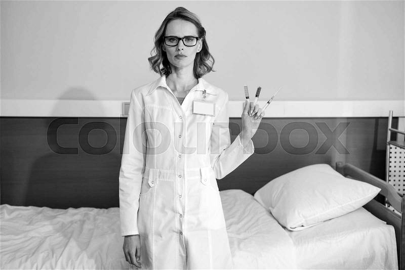 Serious woman doctor holding syringes and looking at camera, black and white photo , stock photo
