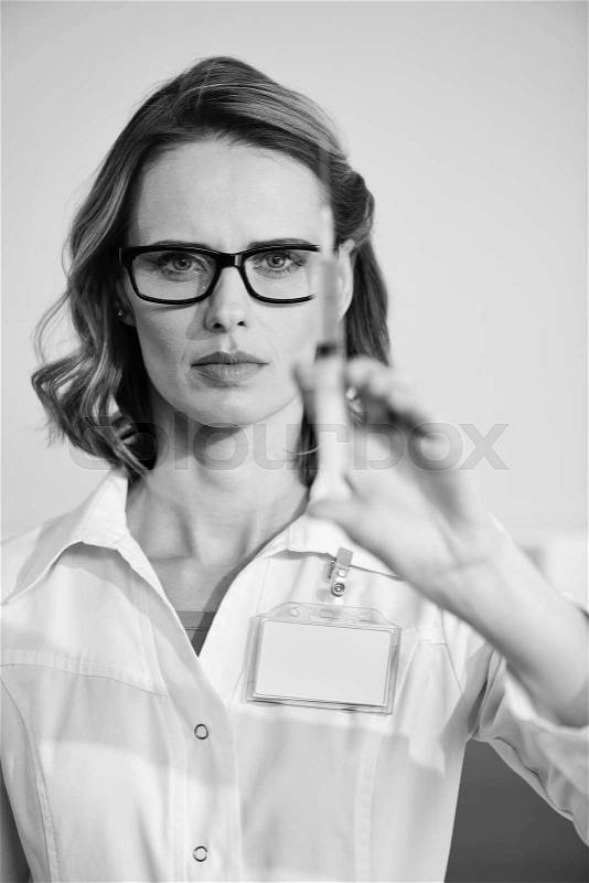 Concentrated woman doctor in eyeglasses holding syringe, black and white photo, stock photo