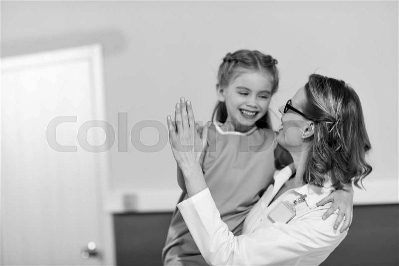 Smiling doctor and happy little girl patient looking at each other, black and white photo, stock photo