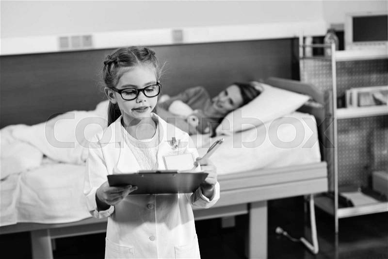 Black and white photo of little girl pretending to be a doctor and writing in clipboard, stock photo