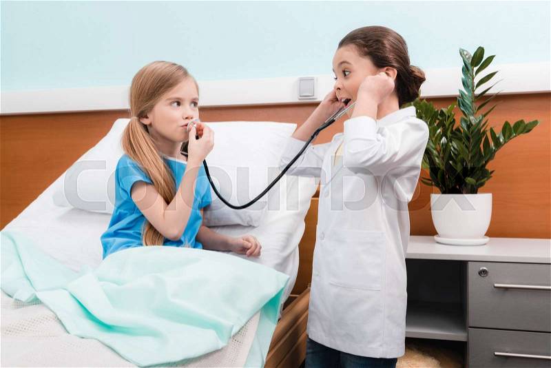Cute little girls playing doctor and patient with stethoscope in hospital, stock photo