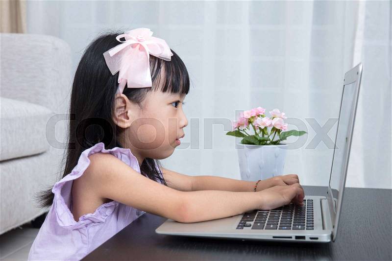 Smiling Asian Chinese little girl using laptop in the living room at home, stock photo