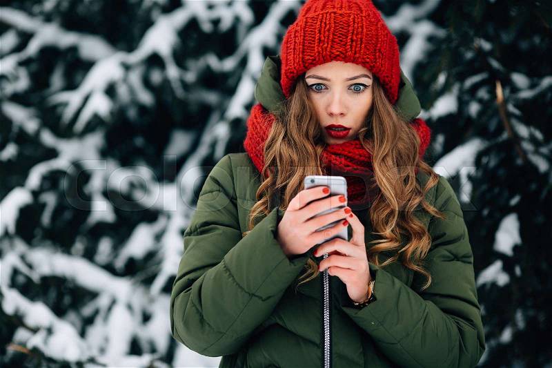 Woman with smartphone. Surprised woman in winter clothes looking at the screen of mobile phone in winter time, stock photo