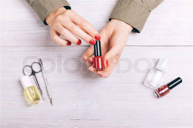 Close-up of a woman holding a manicure red lacquer in hands, top view, stock photo