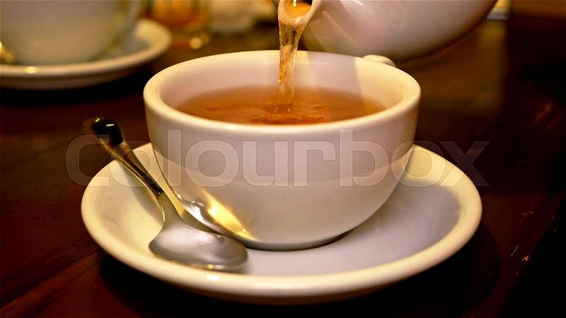 Pouring black tea into cup from teapot. Tea time lunch snack breakfast dinner and supper relax concept, stock photo