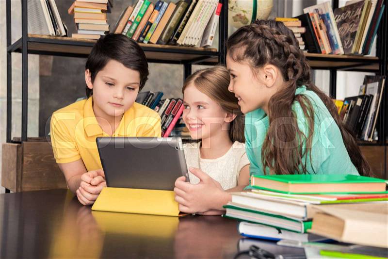 Three smiling schoolchildren using digital tablet in library , stock photo