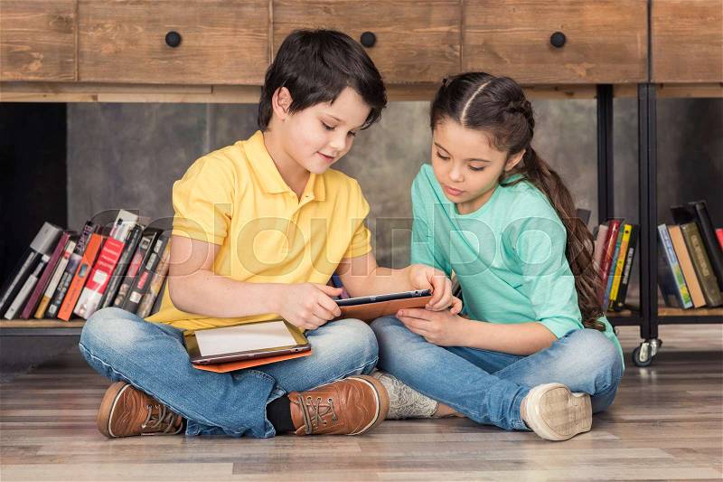 Boy teaching focused girl how to use digital tablets in library, stock photo