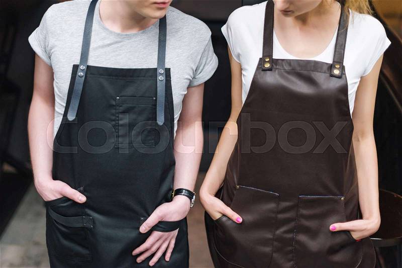 Young chefs or waiters man and woman posing, wearing aprons, stock photo