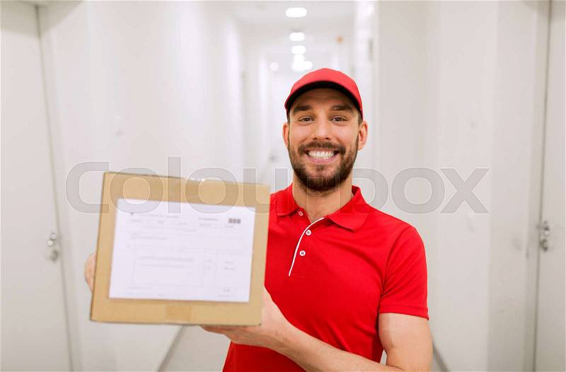 Delivery, mail, people and shipment concept - happy man in red uniform with parcel box in corridor, stock photo