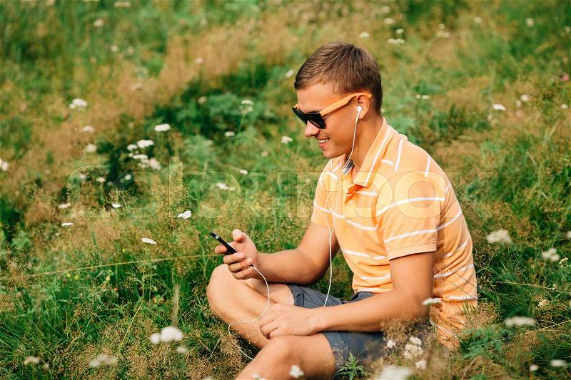 Guy using smart phone. Happy guy smiling with smart phone. Guy listening to music on headphones - communication concept, stock photo
