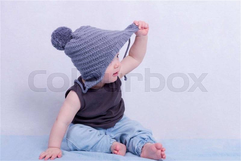 Delightful 10 month toddler boy sitting on the blue carpet and looking away, stock photo