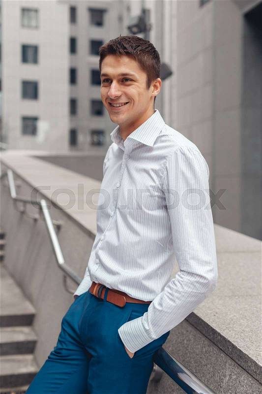 Smiling businessman in formal wear standing outdoors with cityscape in the background. Looking at camera, stock photo