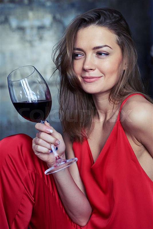 Side view shot of an elated Caucasian girl with a glass of red wine looking sideward. Pretty female holding a glass of red wine in hand. Looking sideward , stock photo