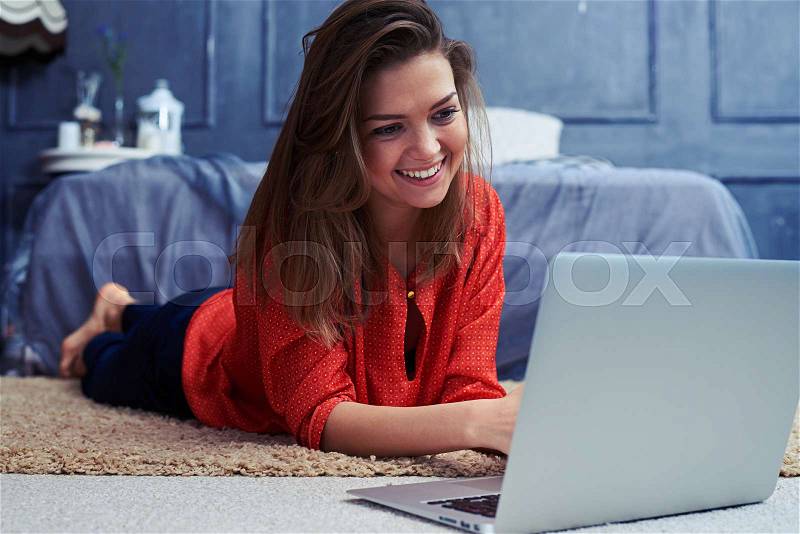 Close-up of beautiful young woman lying on floor and working on a laptop. Caucasian girl looking at the screen of the laptop , stock photo