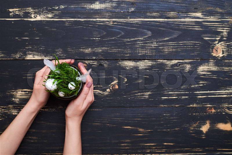 Flat lay picture of flowerpot with green grass and eggs on grunge background. Cropped shot of hands with flowerpot, stock photo