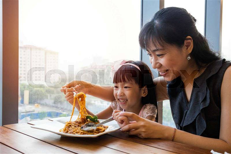Asian Chinese mother and daughter eating spaghetti bolognese in the restaurant, stock photo