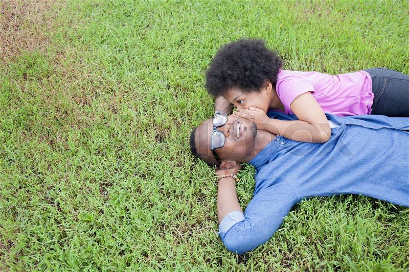 African American father and little kid whispering and gossiping with trust on green grass - with copyspace, stock photo