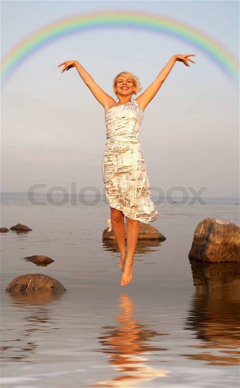 Lovely blond jumping in water under colorful rainbow, stock photo