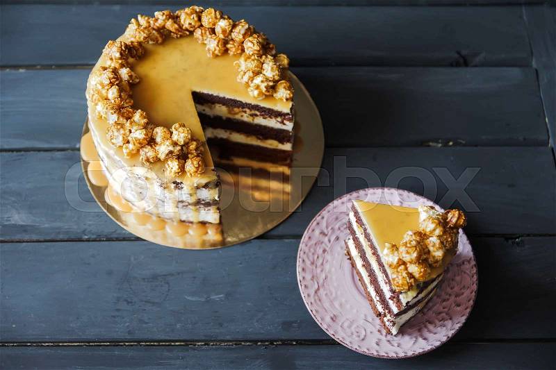 Delicious cake with caramel popcorn and caramel sauce and plate with slace of this cake, stock photo