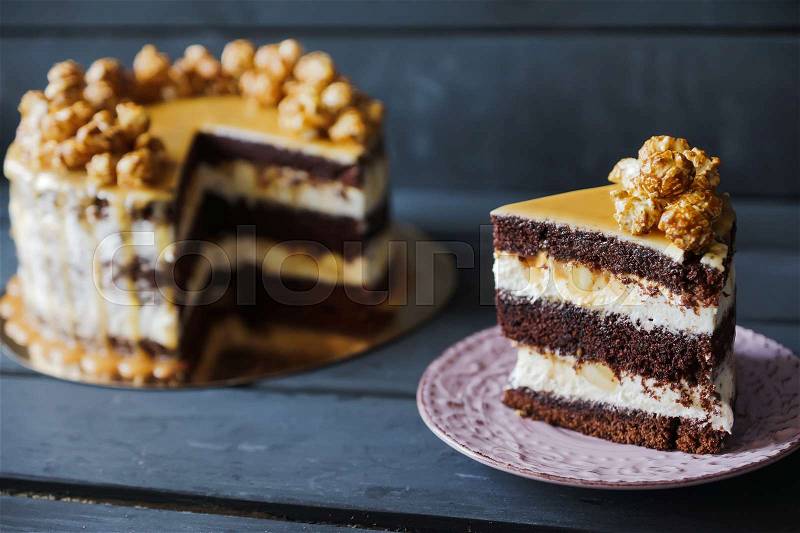 Delicious cake with caramel popcorn and caramel sauce and plate with slace of this cake, stock photo