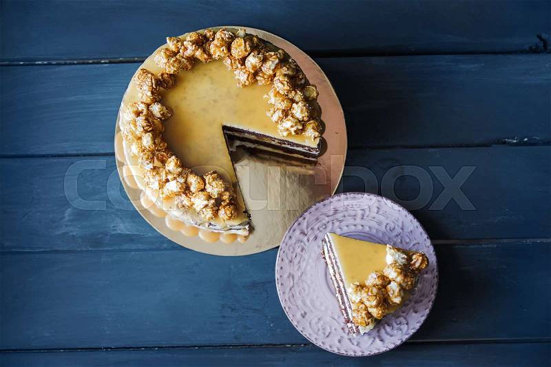 Delicious cake with caramel popcorn and caramel sauce and plate with slace of this cake, top view, stock photo