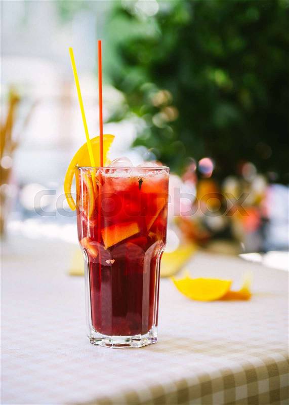 Red cocktail with red and yellow straws , orange wedge and ice in high glass, stock photo