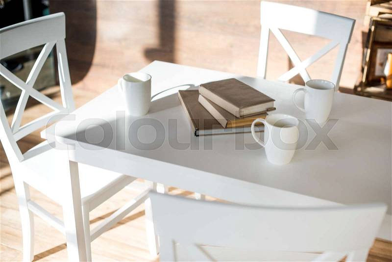 Books stacked on white table near three coffee cups, stock photo