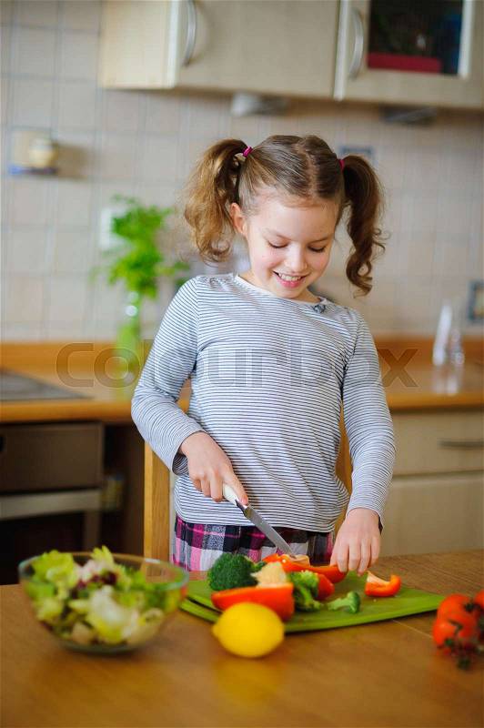 Little cook cooks salad. On a table various vegetables. Lovely girl of younger school age cuts vegetables and greens on a chopping board. Mother\'s assistant diligently prepares, stock photo