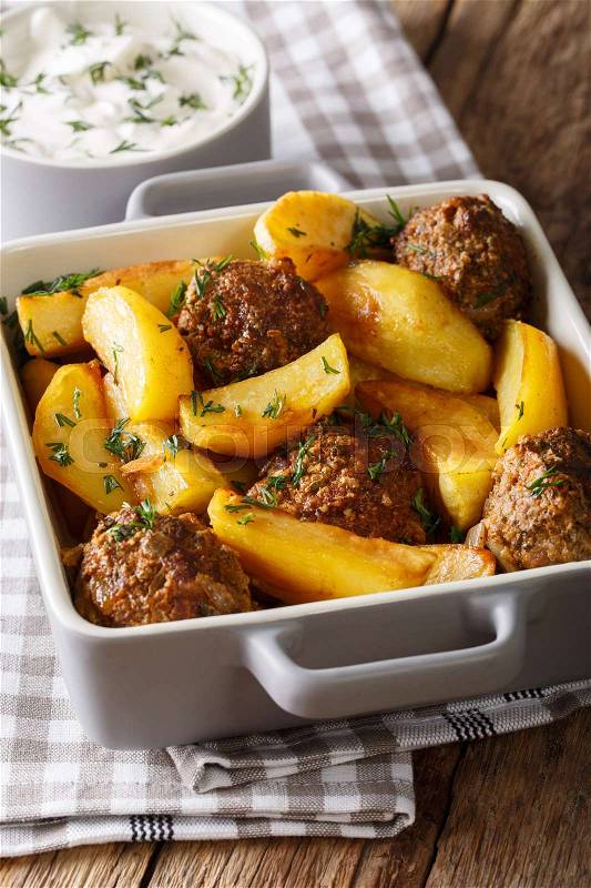 Meat balls with potato wedges in a dish for baking and sour cream close-up on a table. Vertical , stock photo