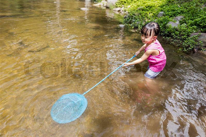 Asian Chinese little girl catching fish with fishing net in the creek, stock photo