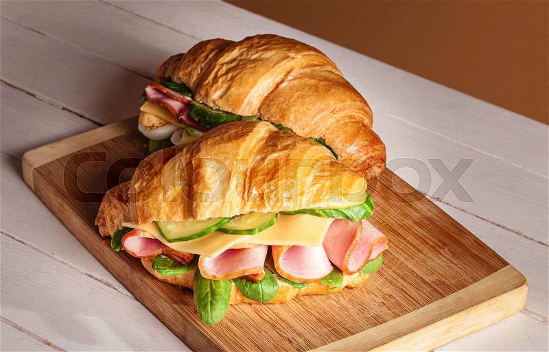 Croissants sandwiches on the wooden cutting board. Selective focus on the front croissant sandwich, stock photo