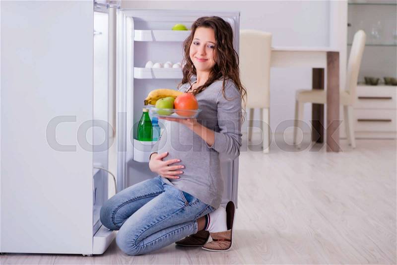 Pregnant woman near fridge looking for food and snacks, stock photo