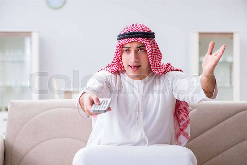 Arab man watching tv at home, stock photo