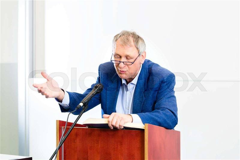 College professor giving lecture and standing at desk, stock photo