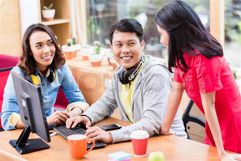 Successful professional team of web designers smiling while testing responsive layout on both mobile phone and desktop PC, stock photo