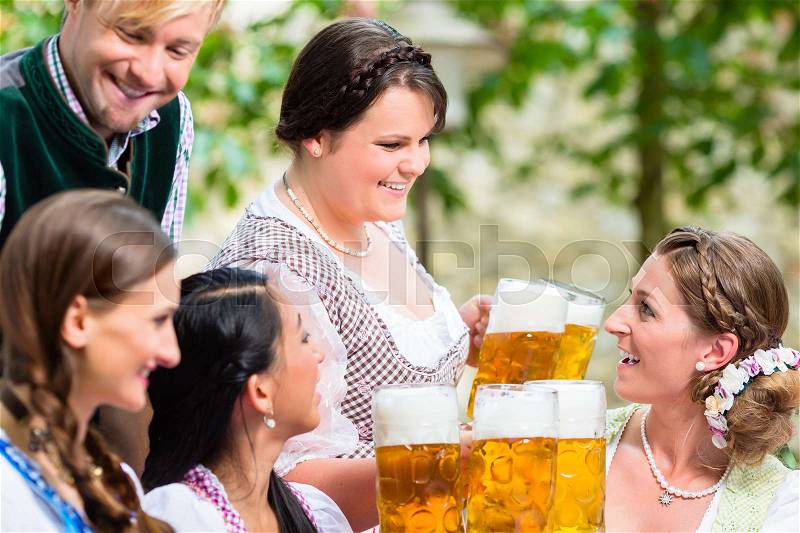 Waitress in beer garden serving drinks to three women and man, stock photo