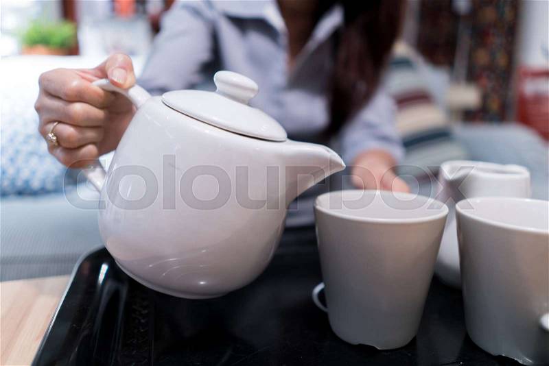 The woman pouring tea or coffee from the white ceramic pitcher put glass on black tray, on time break, concept lifestyle and relaxtime , stock photo