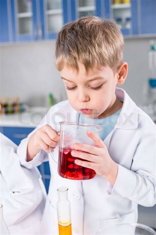 Little boy in lab coat holding flask with reagent in chemical laboratory, stock photo