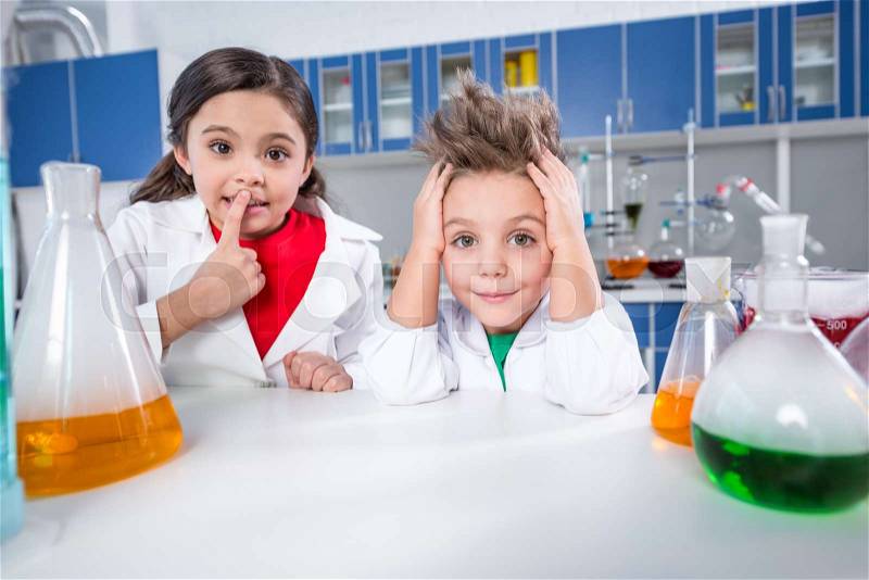Boy and girl in lab coats looking at camera in chemical laboratory, stock photo