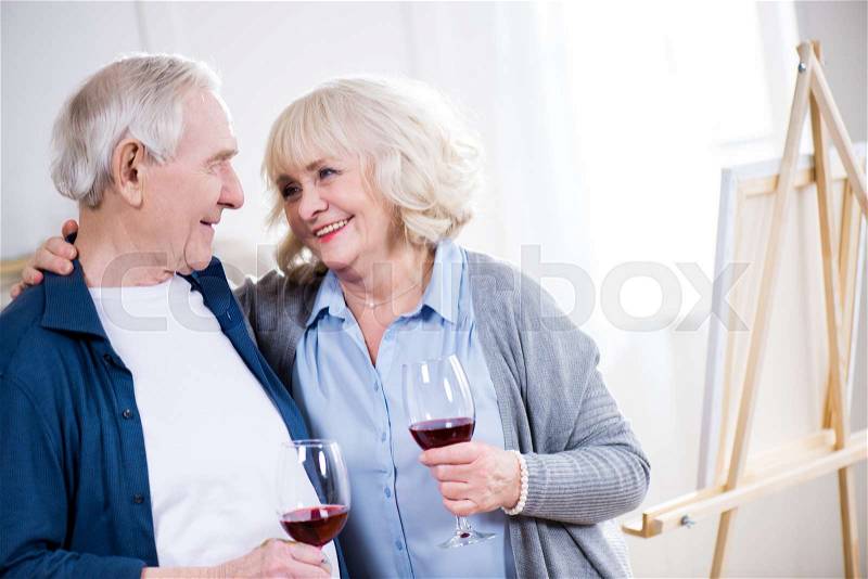 Portrait of smiling senior couple drinking wine in art workshop, stock photo