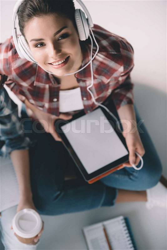 Elevated view of smiling woman listening music in headphones with tablet in hands, stock photo