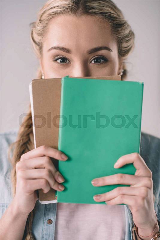 Portrait of woman student covering face with notebooks in hands, stock photo