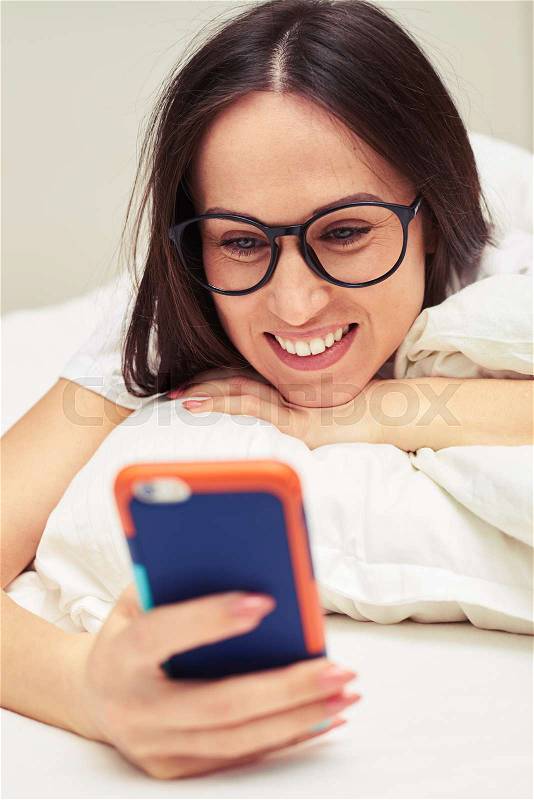 Close-up shot of beautiful female wearing glasses. Reading message on her mobile phone with a delighted. Holding telephone in hands , stock photo
