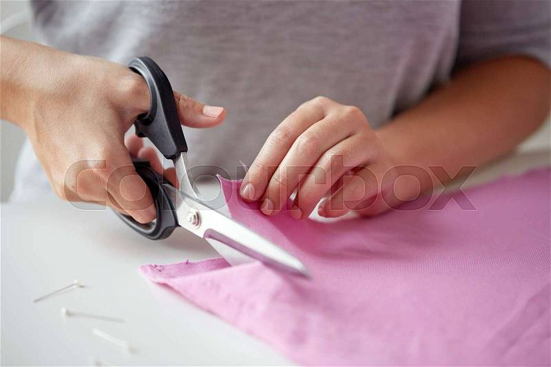 People, stitching, needlework, sewing and tailoring concept - woman with tailor scissors or shears cutting out fabric at studio, stock photo
