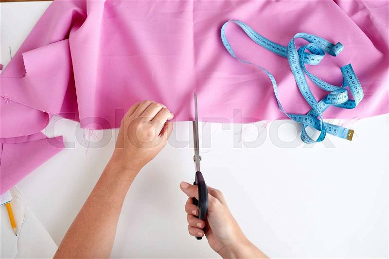 People, stitching, needlework, sewing and tailoring concept - woman with tailor scissors or shears cutting out fabric at studio, stock photo