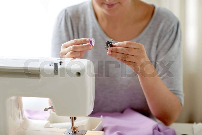 People, needlework and tailoring concept - tailor woman with thread and spool of sewing machine at studio, stock photo