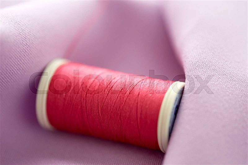 Needlework, craft, sewing and tailoring concept - red thread spool on cloth, stock photo
