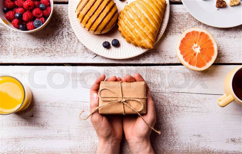 Mothers day composition. Hands of unrecognizable woman holding little gift. Breakfast meal. Studio shot on white wooden background, stock photo