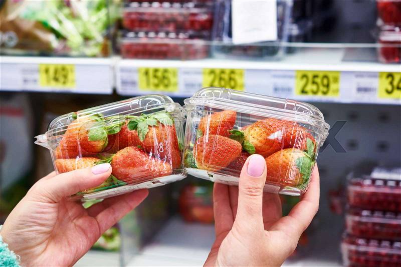 Strawberries in the hands of the buyer at the store on the background of shelves with products, stock photo