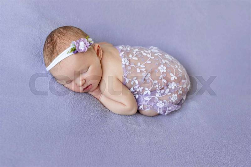 Cute infant sleeping covered with purple veil with flowers on purple soft surface, stock photo